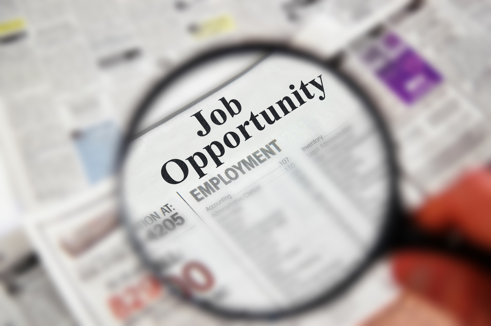 Magnifying glass over a newspaper classified section with "Job Opportunity" text