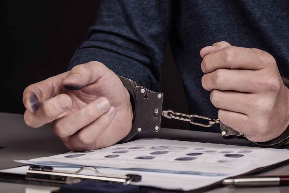 hands with handcuffs lying on top of fingerprint sheets.