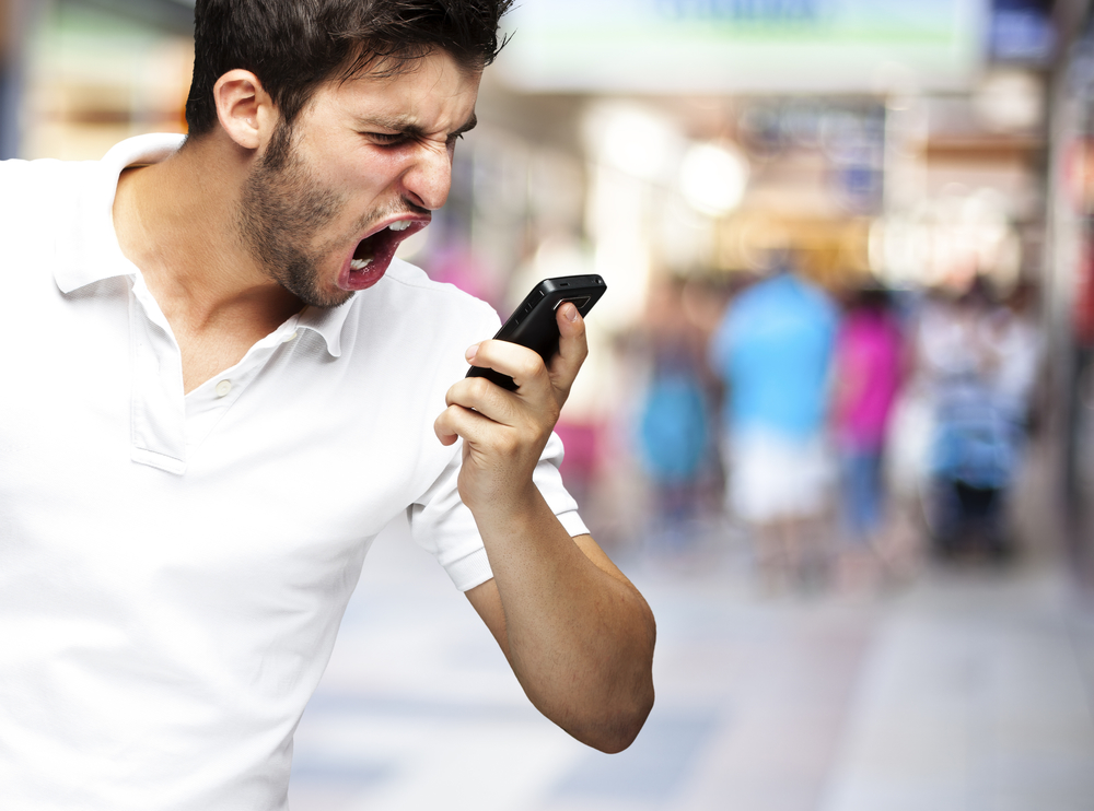 portrait of angry young man shouting using mobile at a crowded m