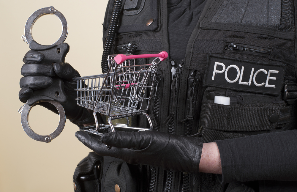 Police officer holding handcuffs and supermarket trolley in concept of shoplifting