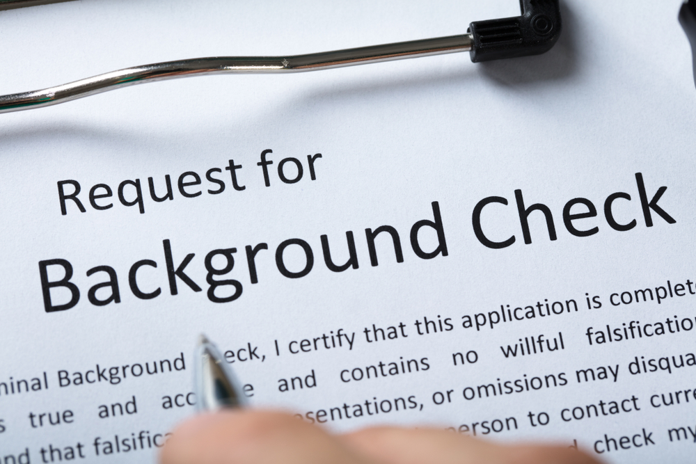a background check form on a clipboard while someone hovers over it with a pen