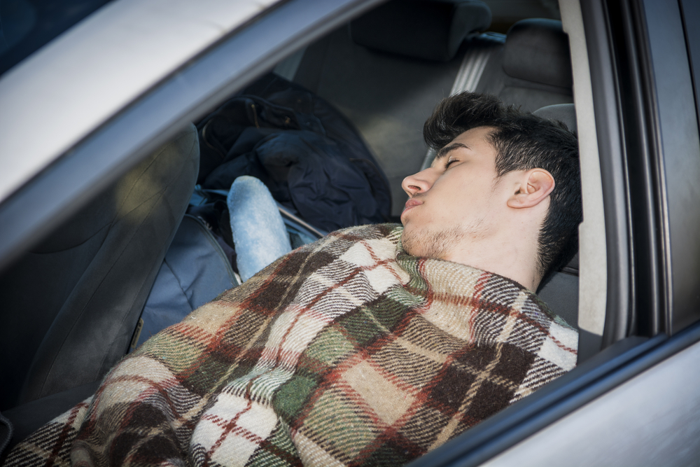 man sleeping in car with blanket draped over him