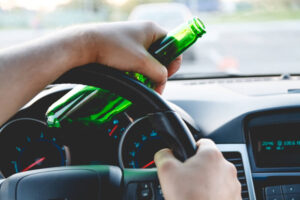 Drunk young man driving a car with a bottle of beer. 