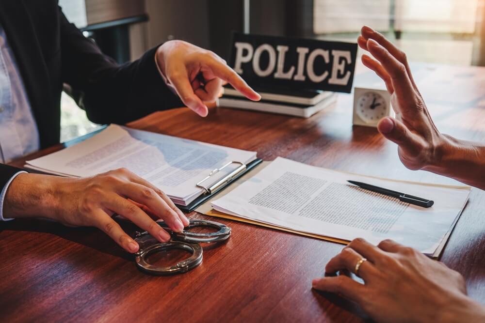 Law enforcement officer interrogating Criminals male with handcuffs in the investigation room.